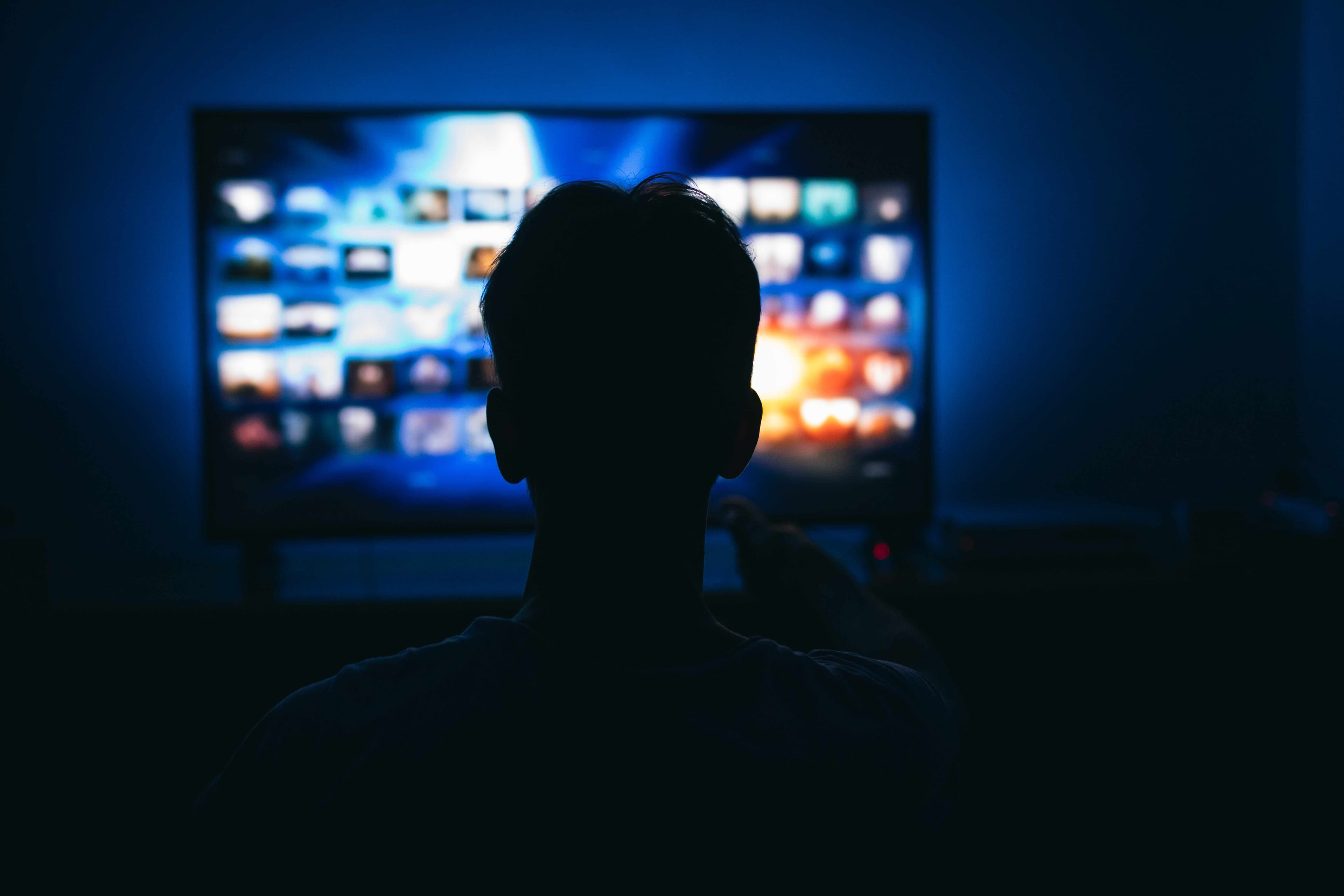 Silhouette einer Person, die in einem dunklen Raum fernsieht, mit einer Streaming-Dienst-Oberfläche auf dem Bildschirm. Warum Connected TV jetzt zählt – Trends, Daten & Wachstum im Überblick. viiew.de powered by esome advertising technologies GmbH.